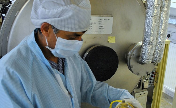 A researcher in cleanroom clothing working at a vacuum chamber in a laboratory